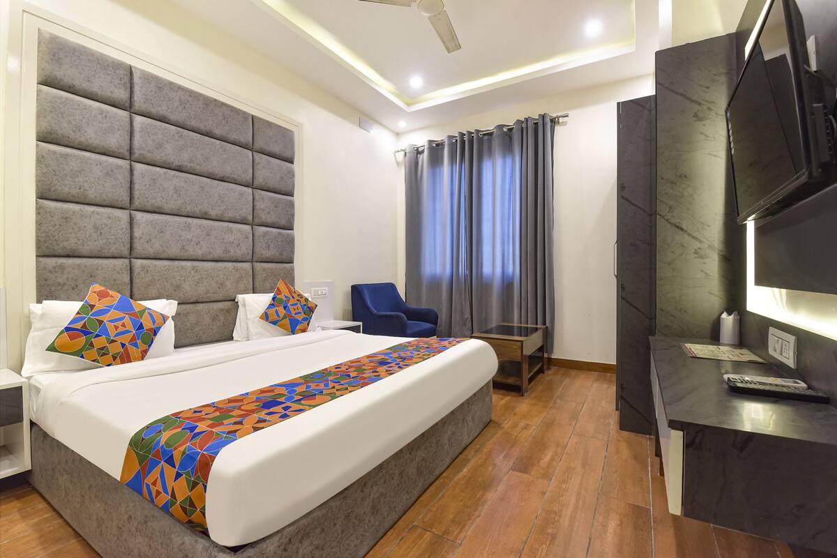 A modern hotel room with a large bed, a desk, a chair, and a television.