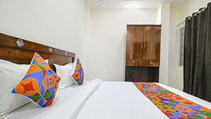 A hotel room with a wooden headboard, a bed with white linens, colorful pillows, and a geometric-patterned bedspread. - Fabhotel Dr Greens (Indore)