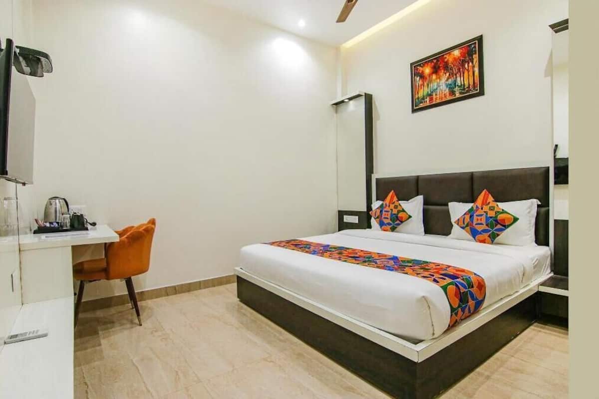 A hotel room with a bed, a desk, a chair, a mirror, and a painting on the wall.