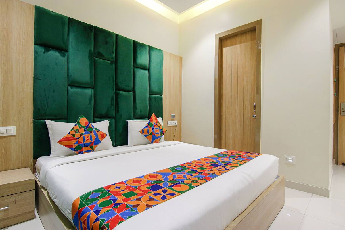 A modern bedroom with a large bed, green upholstered headboard, and colorful geometric-patterned bed runner.