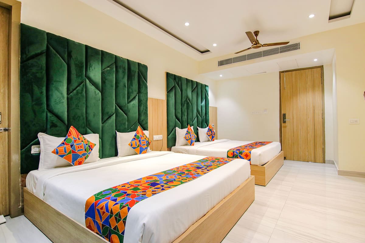 A hotel room with two beds, a green headboard, a ceiling fan, and a wooden door.