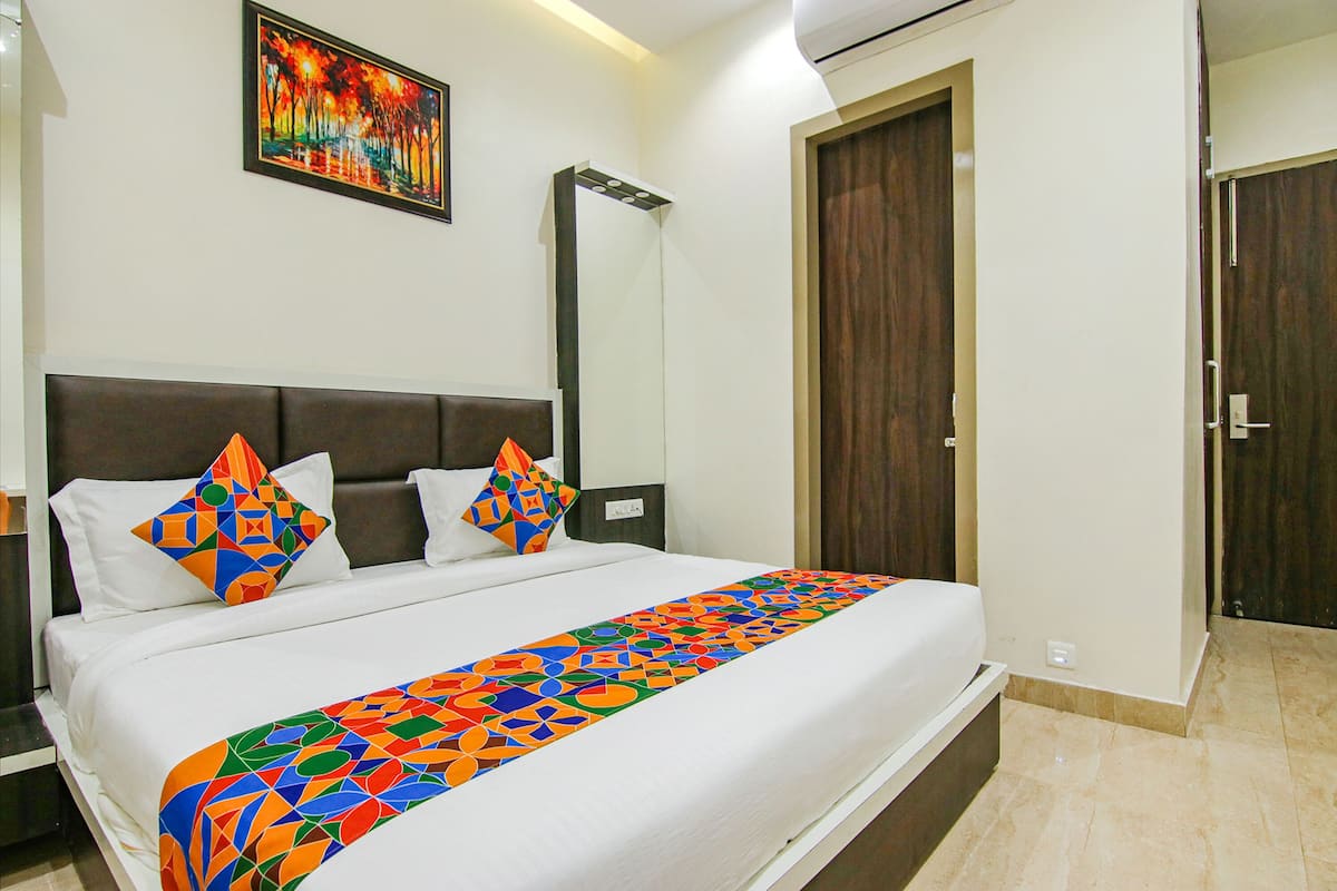 A hotel room with a large bed, a headboard, a painting on the wall, and a door.