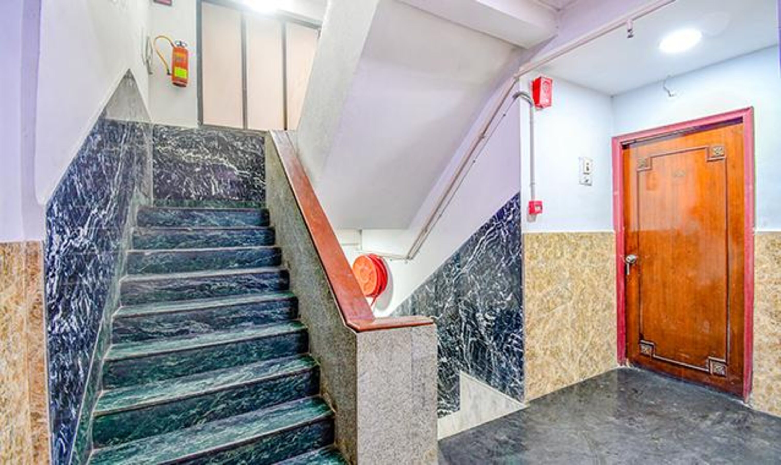 A staircase with marble steps leading to a landing, a wooden door, and a fire extinguisher on the wall.