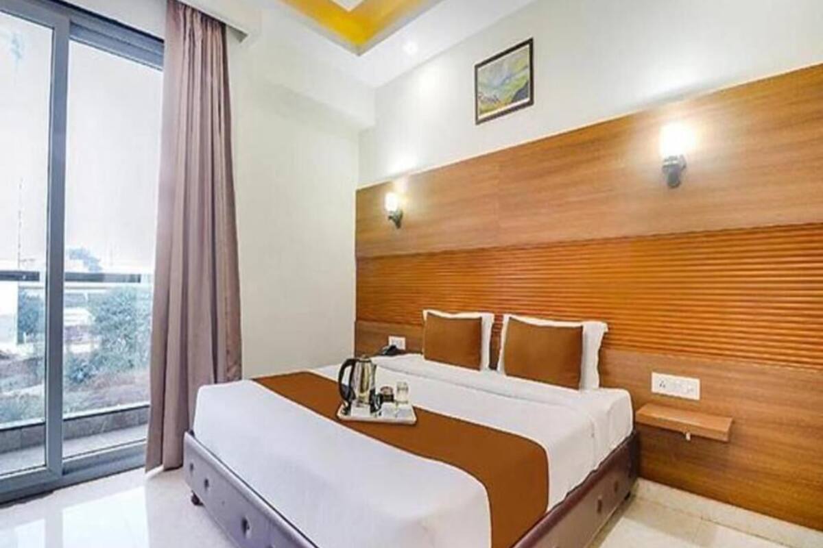 Habitación de hotel con una cama grande, cabecero de madera, mesita de noche y una ventana con cortinas.
