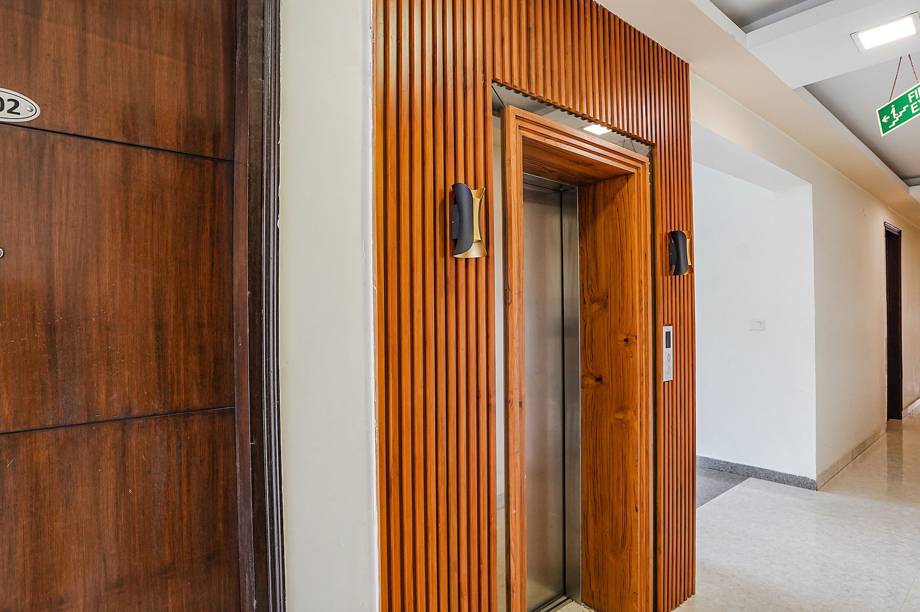 A hallway with a wooden panel wall, an elevator, and a door with a number plate.