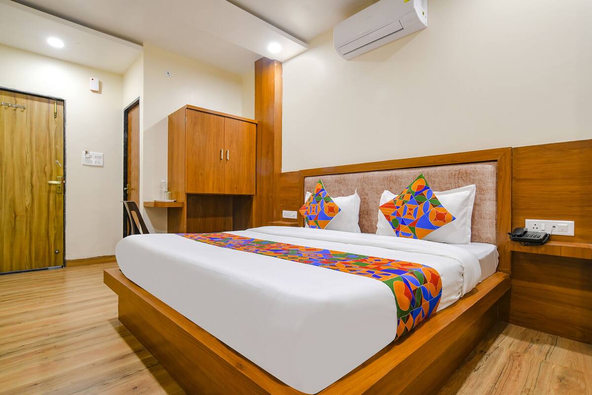 Una cama bien tendida con una colcha de diseño geométrico y colores vivos, un cabecero de madera y una mesita de noche con un teléfono.