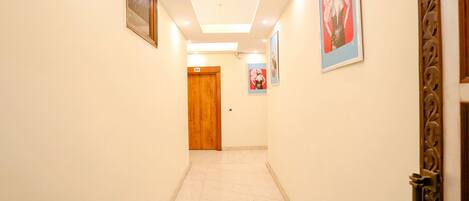 A hallway with a wooden door at the end, a ceiling light, and framed pictures on the walls.