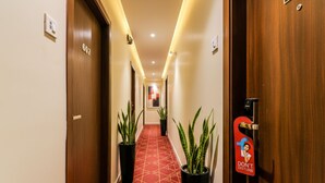 A hotel hallway with a red patterned carpet, wooden doors, and potted plants. - FabHotel Ascot International (Mumbai)