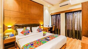 A hotel room with a wooden headboard, a bed with colorful bedding, a bedside table with a lamp, and a window with curtains. - FabHotel Ascot International (Mumbai)