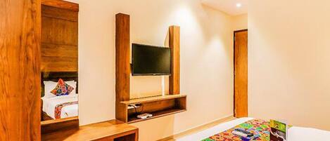 Una habitación de hotel con una cama, un televisor montado en la pared y un banco de madera.