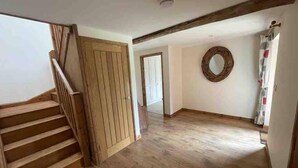 A spacious room with wooden flooring, a wooden staircase, and a door leading to another area. - Charming Norfolk Barn Conversion in Barnham Broom (Norwich)