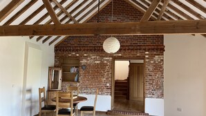 A spacious room with exposed wooden beams, a brick wall, and a wooden table with chairs. - Charming Norfolk Barn Conversion in Barnham Broom (Norwich)