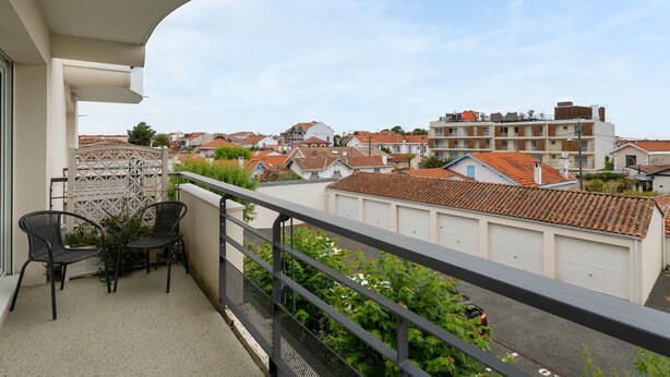 A balcony with a view of residential buildings, a gated entrance, and outdoor furniture. - Quiet T2 Apartment in Arcachon with Private Parking, Terrace, and Close to Beach and Shops (Arcachon)