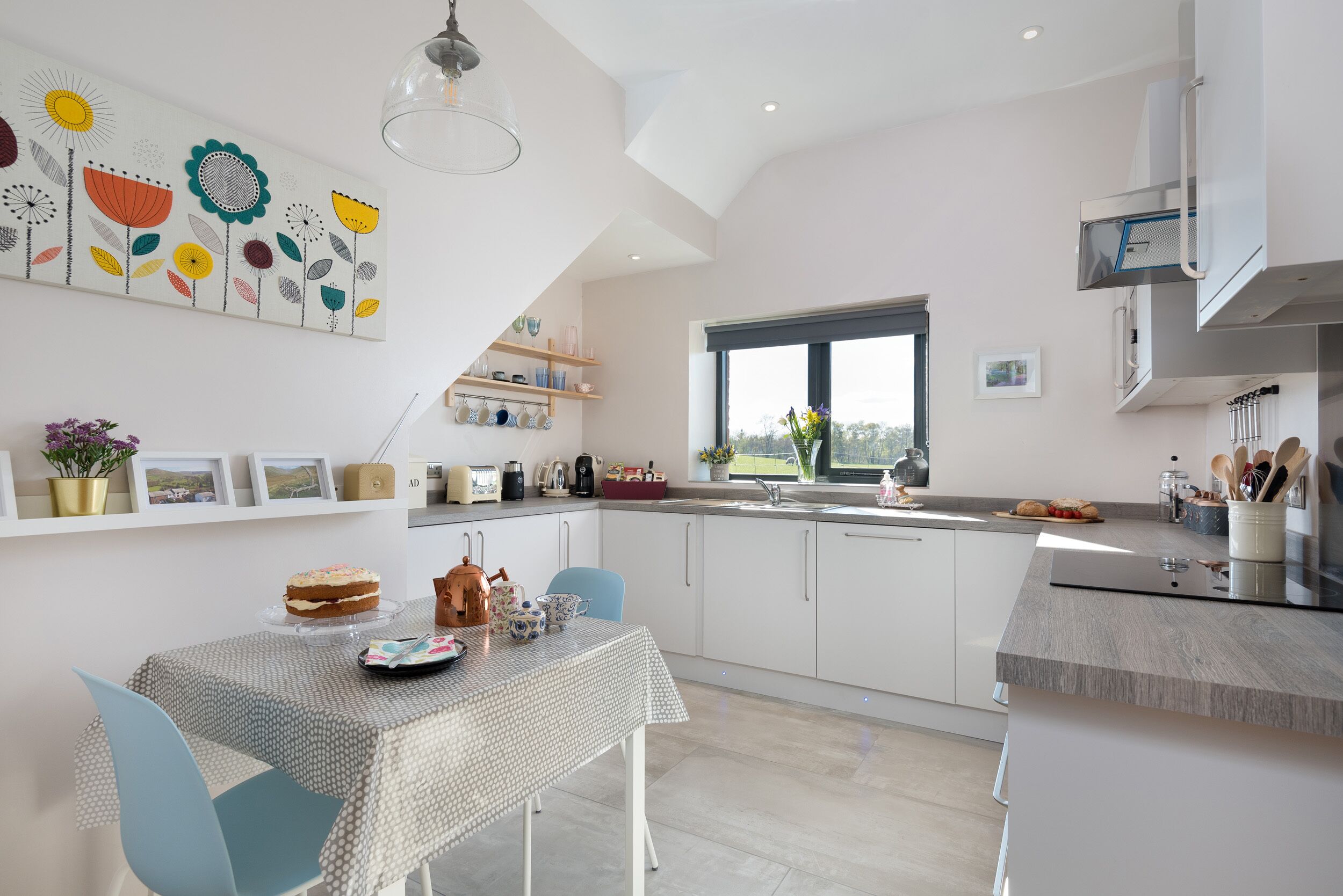 A modern kitchen with white cabinetry, a dining table with a polka dot tablecloth, and a large window.