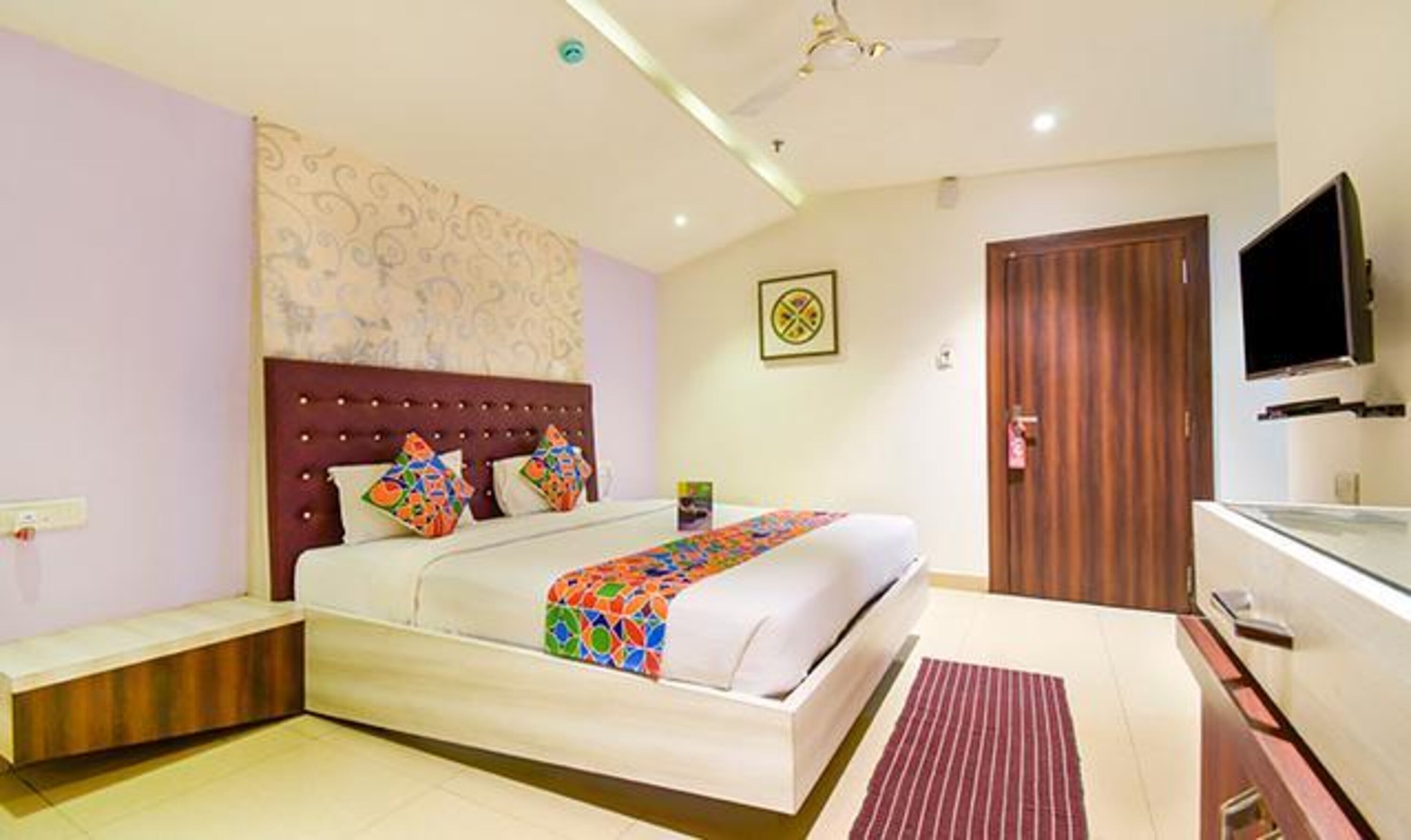 A bedroom with a bed, a TV, a wooden cabinet, and a ceiling fan.