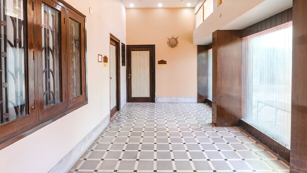 A corridor with a checkered floor, wooden cabinets with glass doors, and a door with a decorative emblem. - Fabhotel Harmony (Prayagraj)