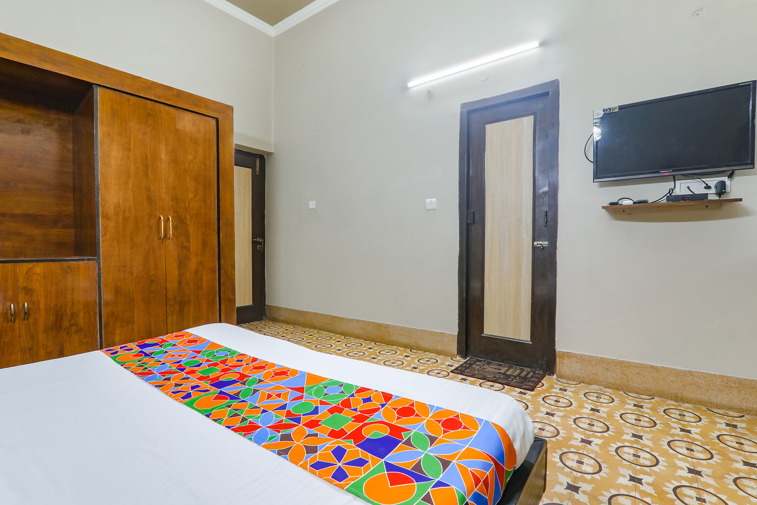 A room with a bed, a wardrobe, a television mounted on the wall, and a patterned floor.