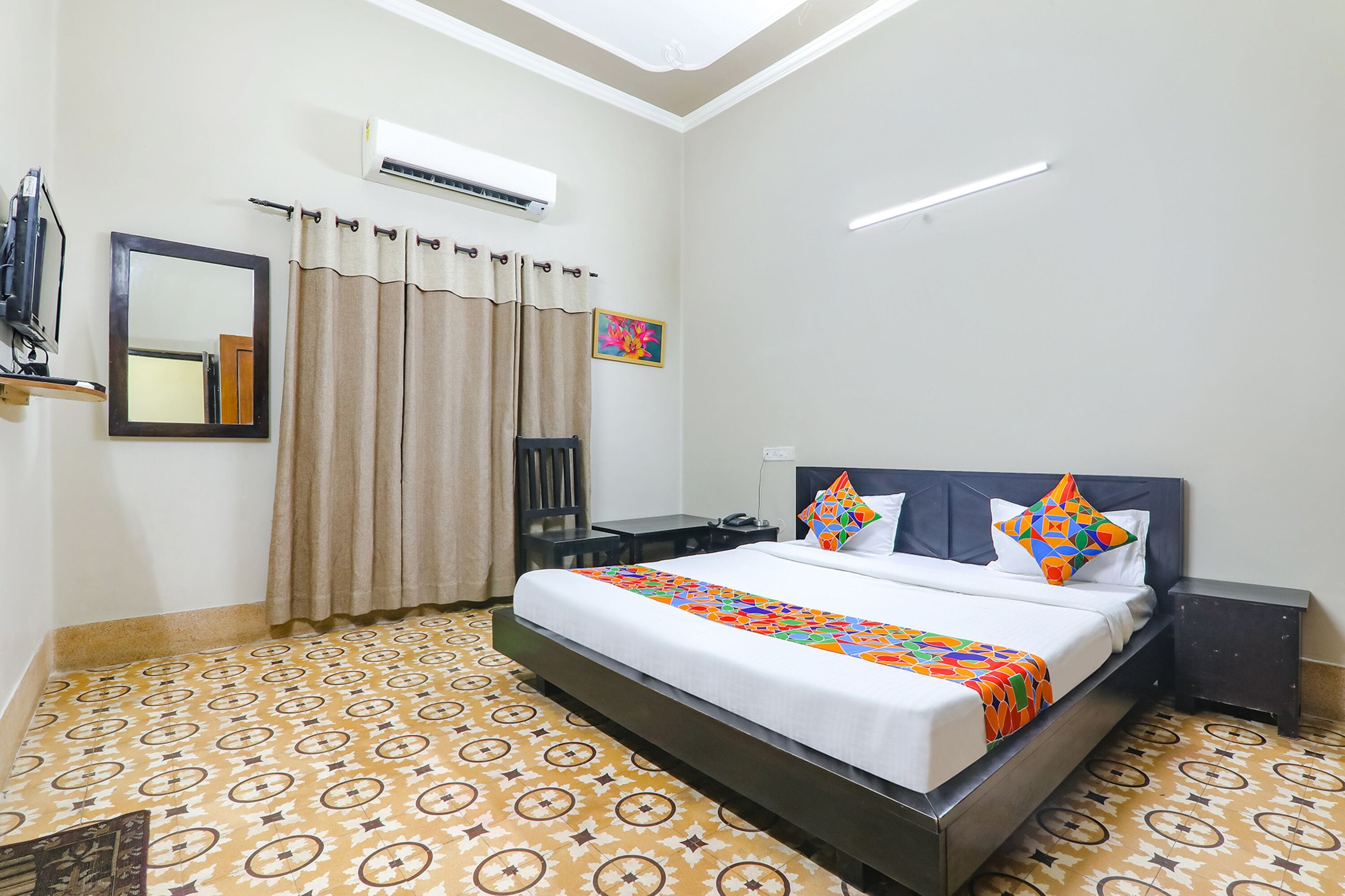 A neatly arranged hotel room with a bed, bedside tables, a mirror, and an air conditioning unit.