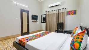 A hotel room with a bed, a TV, an air conditioner, a chair, and a painting on the wall. - Fabhotel Harmony (Prayagraj)