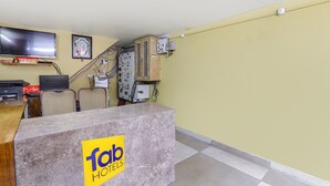 A hotel reception area with a reception desk, a television, a framed picture on the wall, and electrical equipment. - Fabhotel Harmony (Prayagraj)