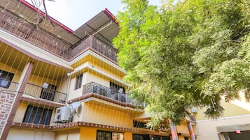 A multi-story building with balconies, a tree in front, and a building with a yellow facade.