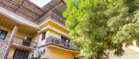 A multi-story building with balconies, a tree in front, and a building with a yellow facade.