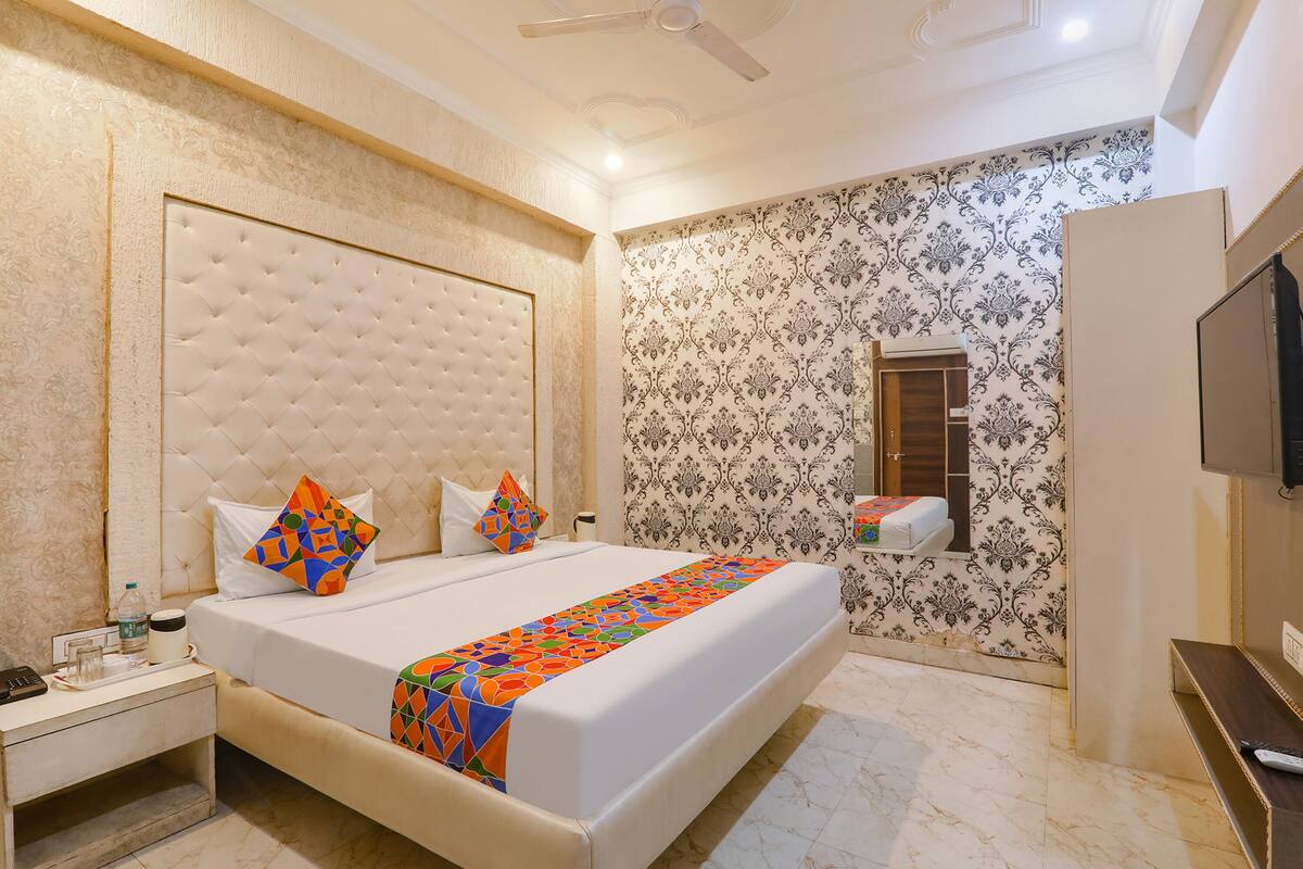 A hotel room with a large bed, a bedside table, a mirror, and a TV.