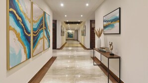 A hallway with marble flooring, framed artwork on the walls, and a console table with books and decorative items. - Fabhotel Triveni (Prayagraj)