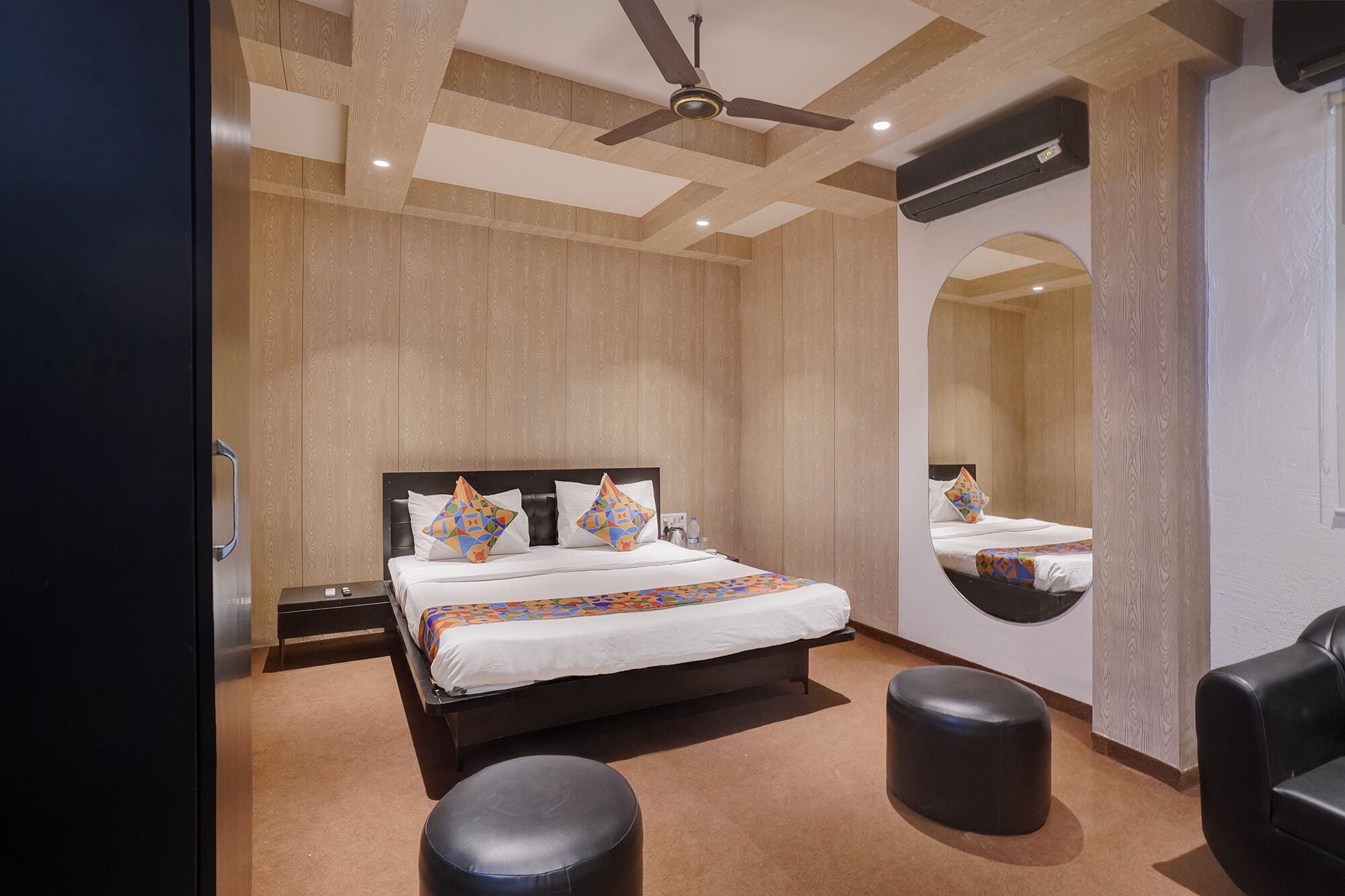 A modern hotel room with a large bed, a ceiling fan, a mirror, and a seating area.