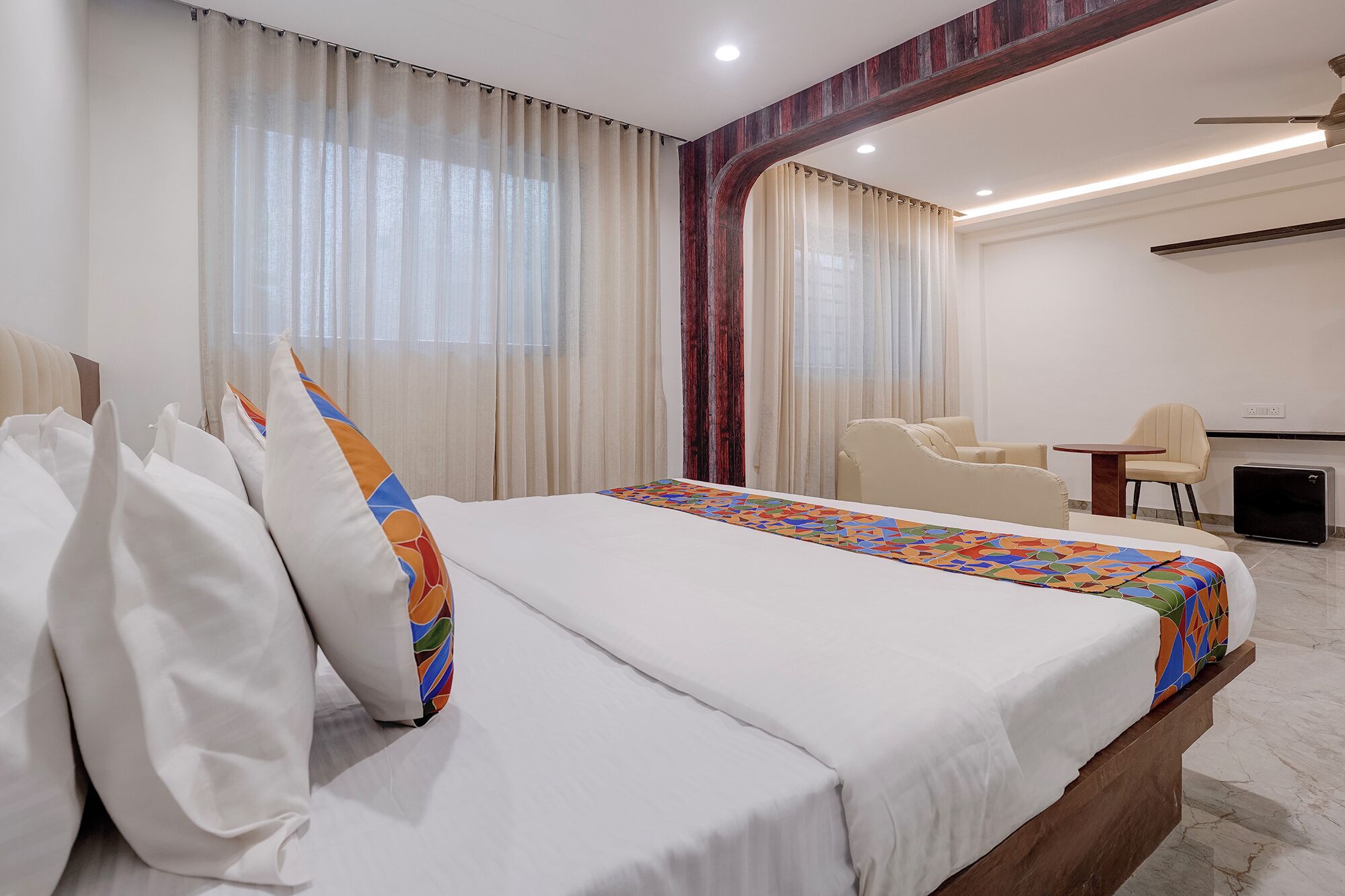 Una habitación de hotel con una cama, un escritorio, una silla y un amplio ventanal con cortinas.