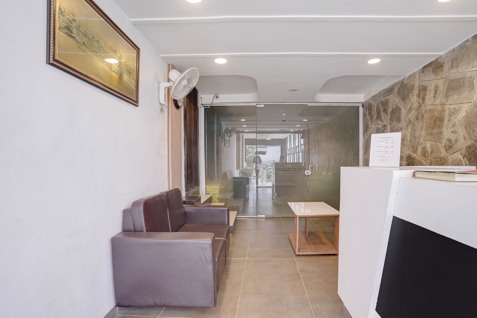 A reception area with a reception desk, seating area with chairs, a fan, and a framed picture on the wall.