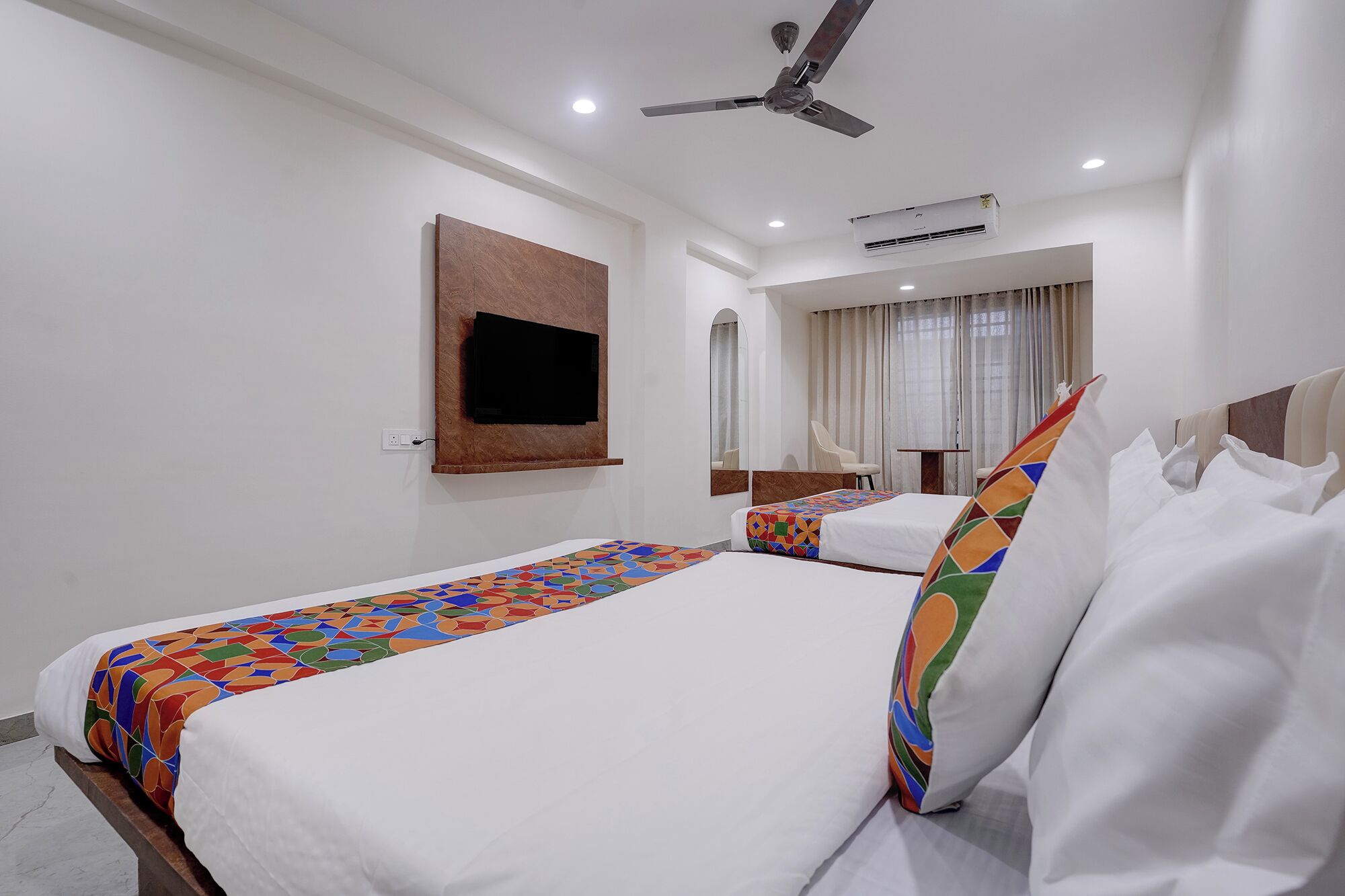 A hotel room with a bed, a TV mounted on the wall, a ceiling fan, and an air conditioning unit.