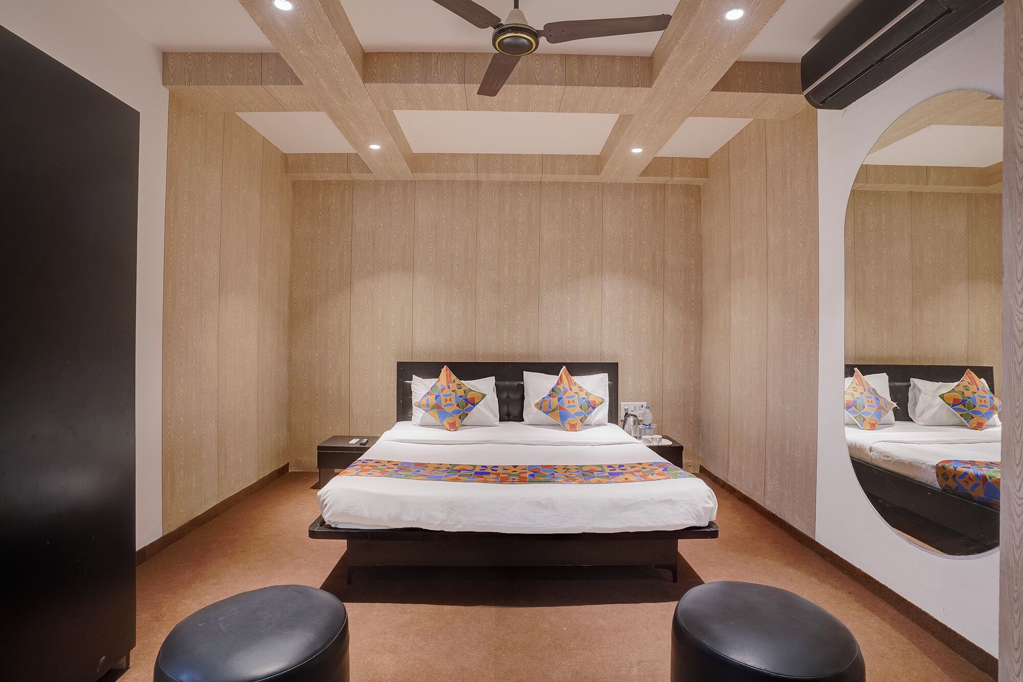 Un dormitorio con una cama, dos mesitas de noche, un ventilador de techo, un espejo grande y suelo alfombrado.