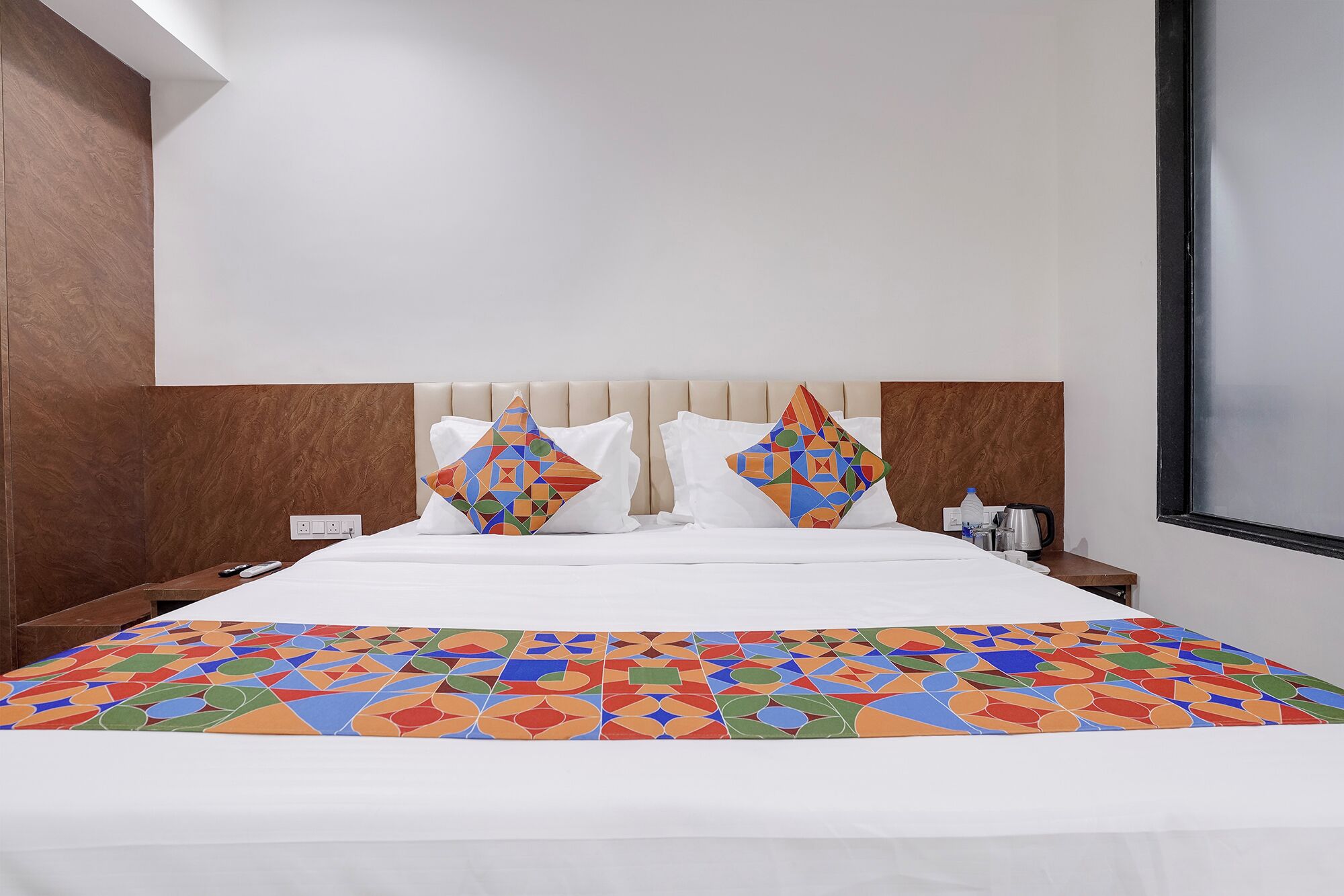 Une chambre d’hôtel avec un lit, deux oreillers, une table de chevet, une fenêtre et un mur recouvert d’un panneau en bois.