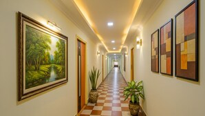 Un pasillo de hotel con piso a cuadros, obras de arte enmarcadas en las paredes y plantas en macetas.