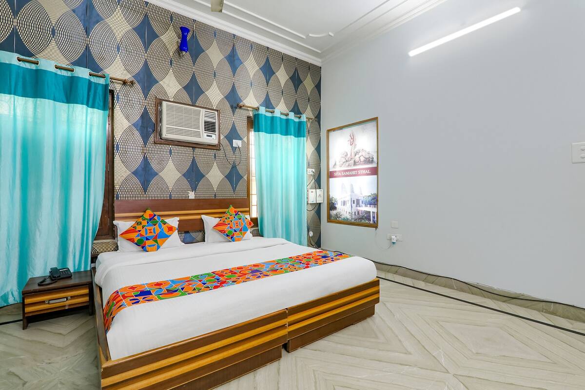 Ein Hotelzimmer mit Bett, Vorhängen, einer Wand-Klimaanlage, einem gerahmten Bild und einer Wand mit Muster.