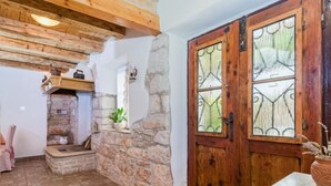 Un interior rústico con vigas de madera a la vista, pared de piedra, puerta de madera con vidrieras y suelo de baldosas.