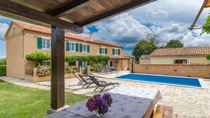 Un espacio al aire libre techado con piscina, sillones de descanso y una mesa decorada con flores.
