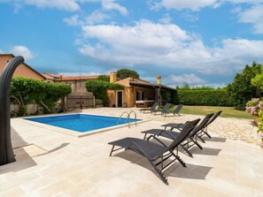 Una piscina con sillas de descanso y un porche cubierto.