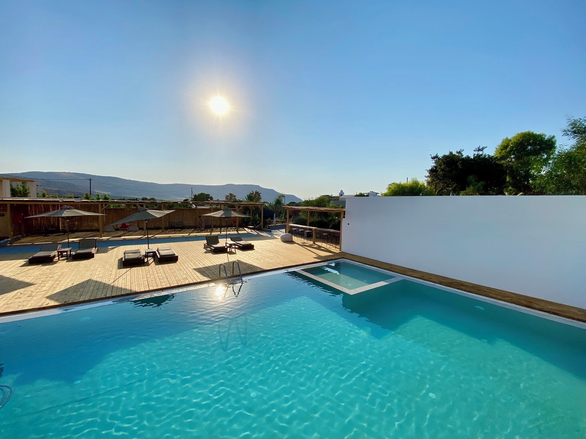 A rooftop pool with clear blue water, sun, and mountains in the background.