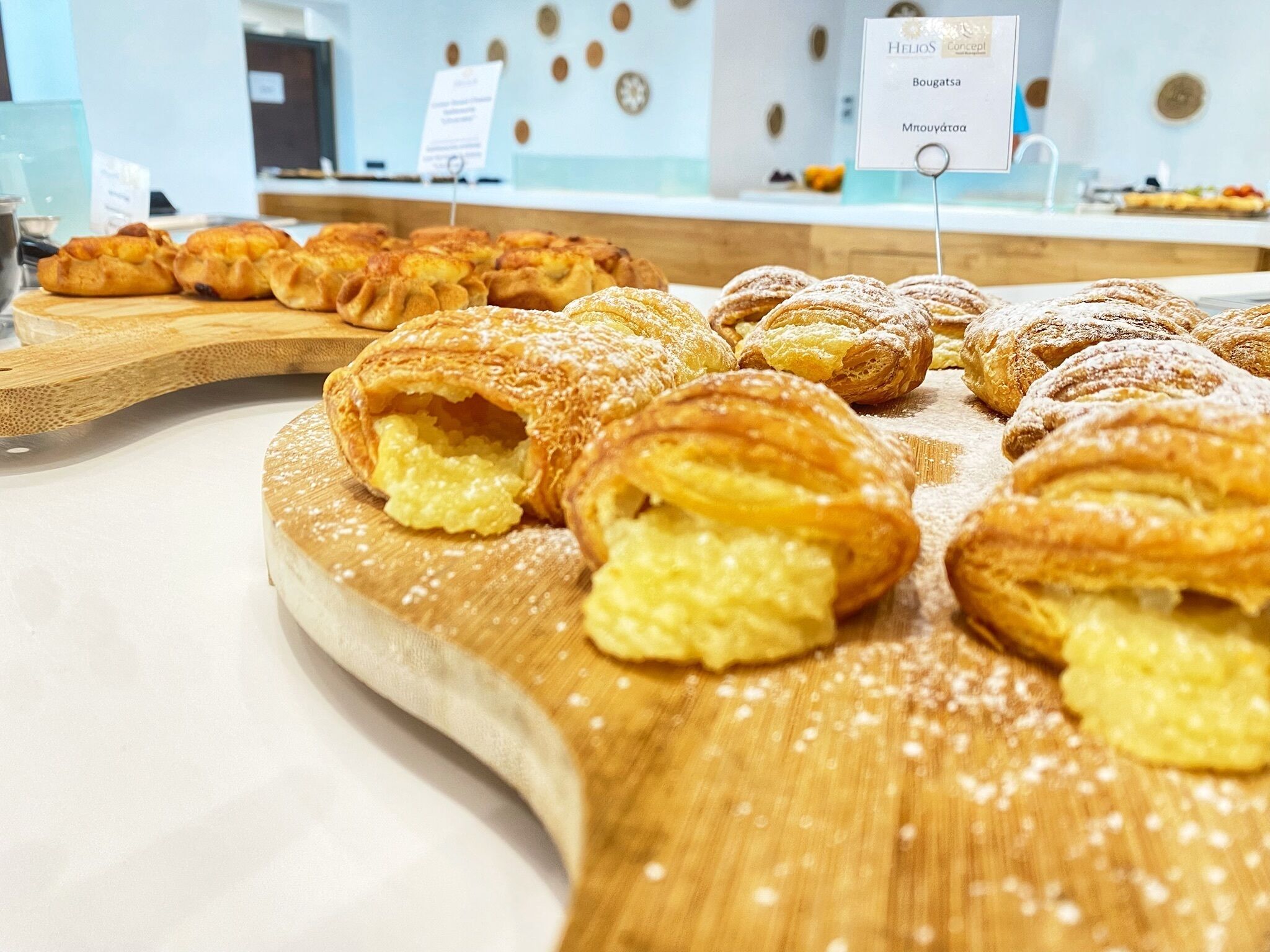 Una vitrina de pastelería con diversos productos de repostería, incluyendo cruasanes y un letrero que indica un concepto llamado 'Helios'.