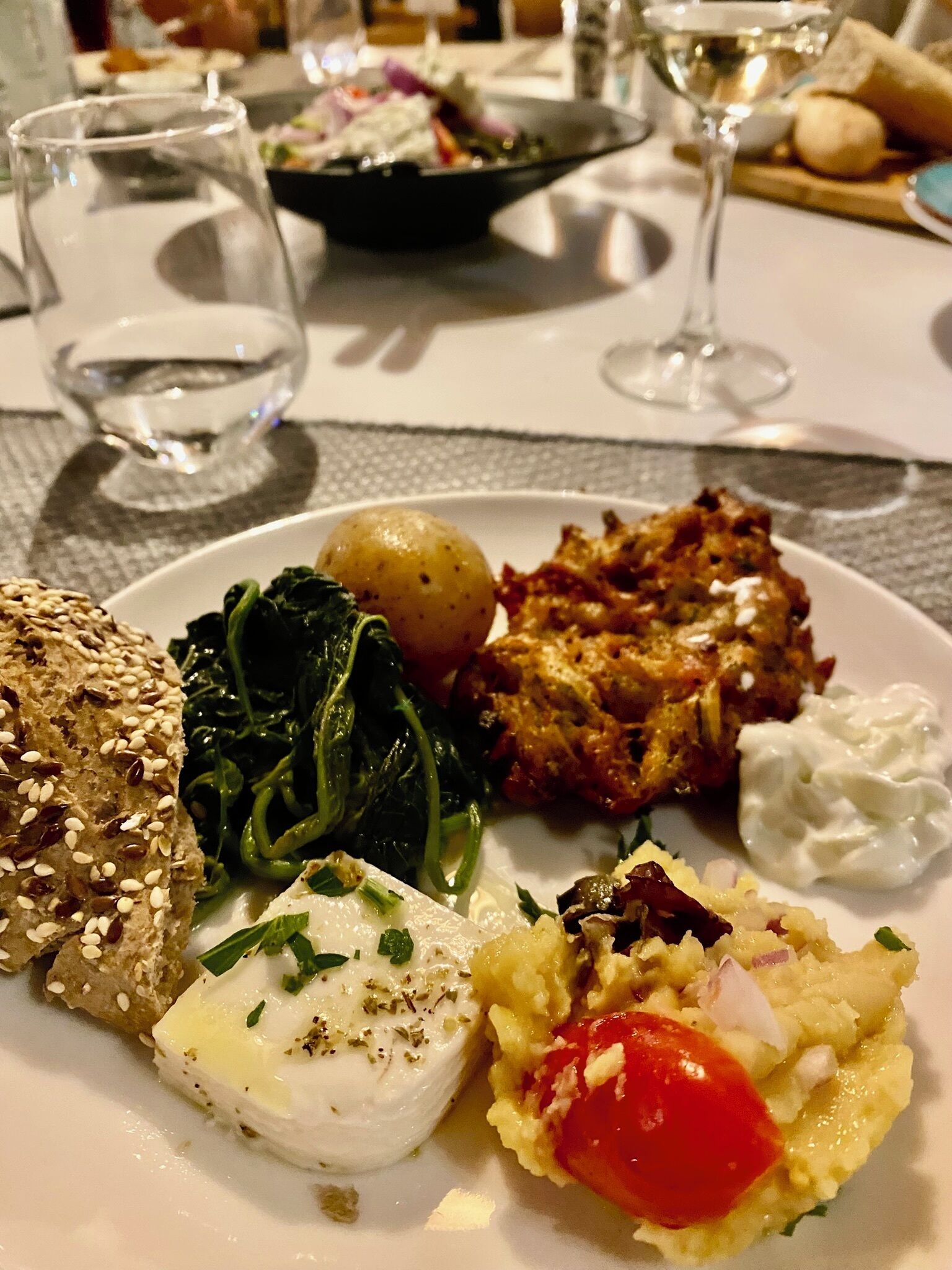 A plate of food with various items including a slice of bread, greens, potatoes, and a creamy dish.