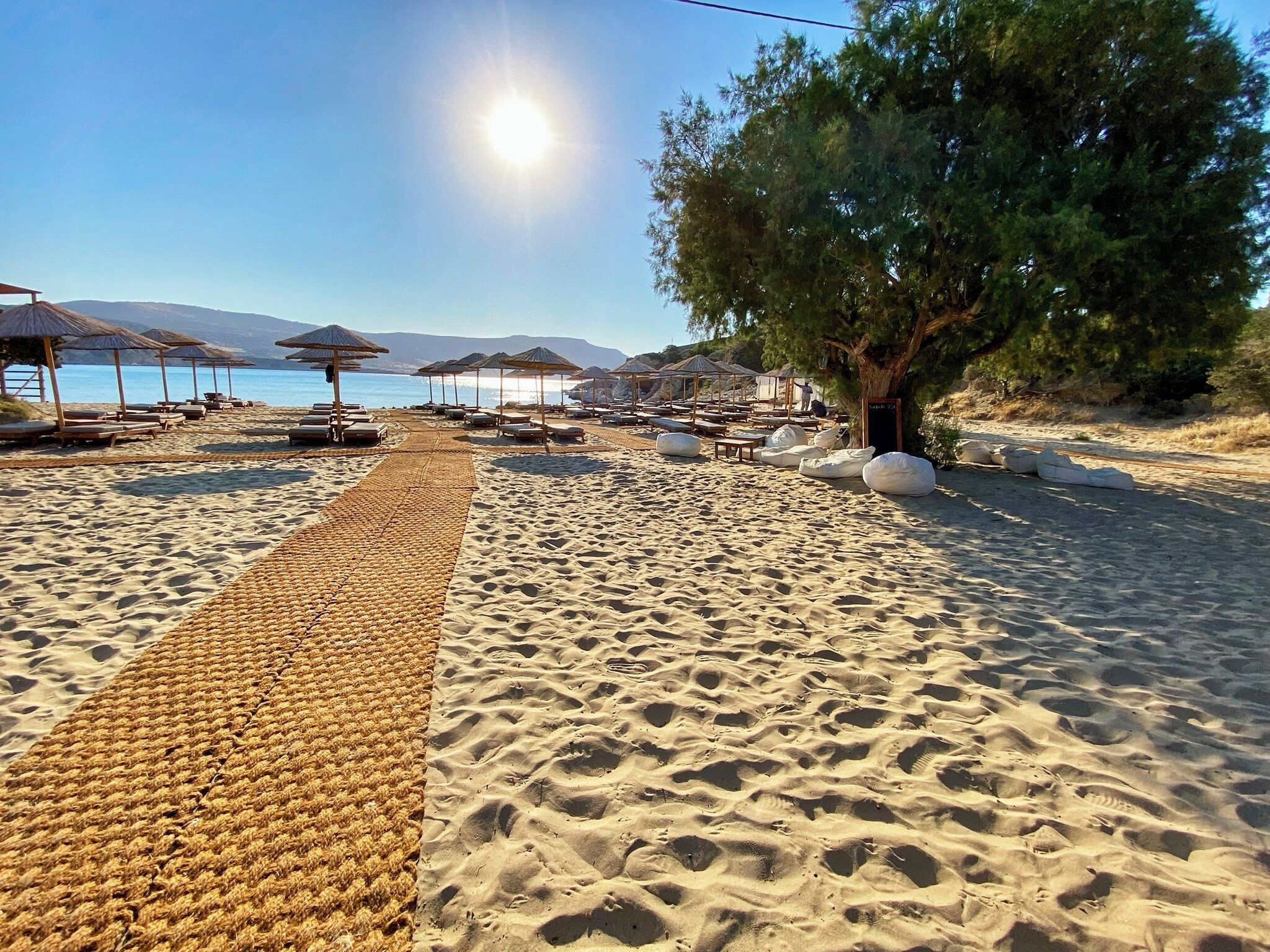 A beach with sun loungers, umbrellas, and a walking path.