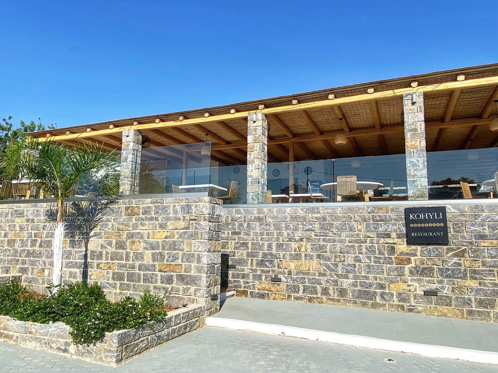 Un edificio de piedra con un letrero que dice 'Kohyli Restaurant' y un área de estar al aire libre cubierta.