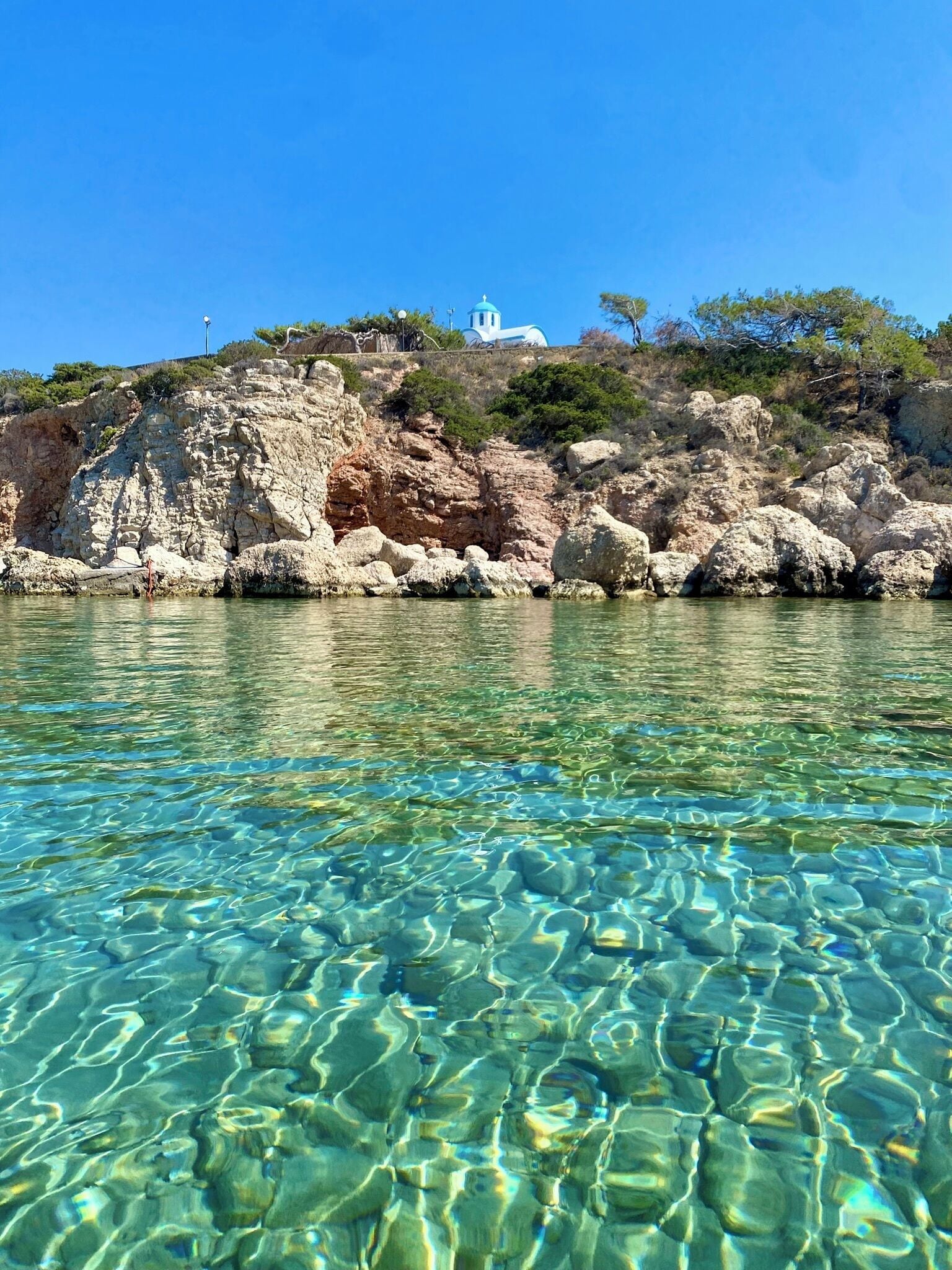 Clear coastal waters with rocky terrain and a white building on a hill.