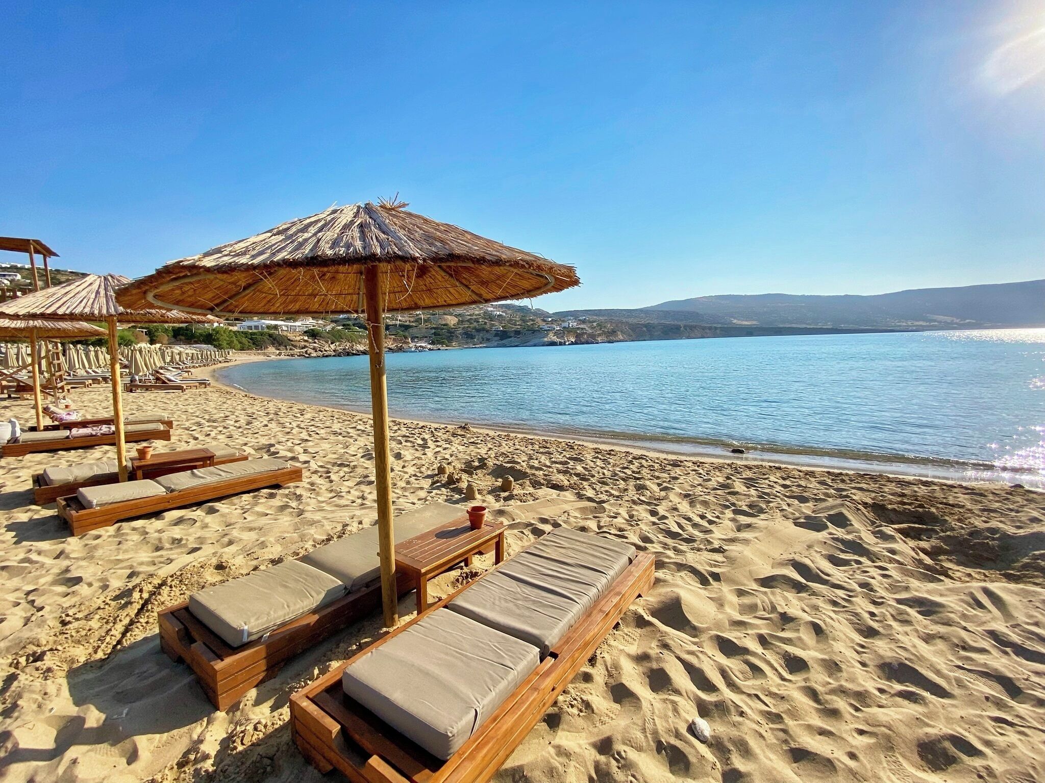 A beach with wooden lounge chairs and thatched umbrellas.