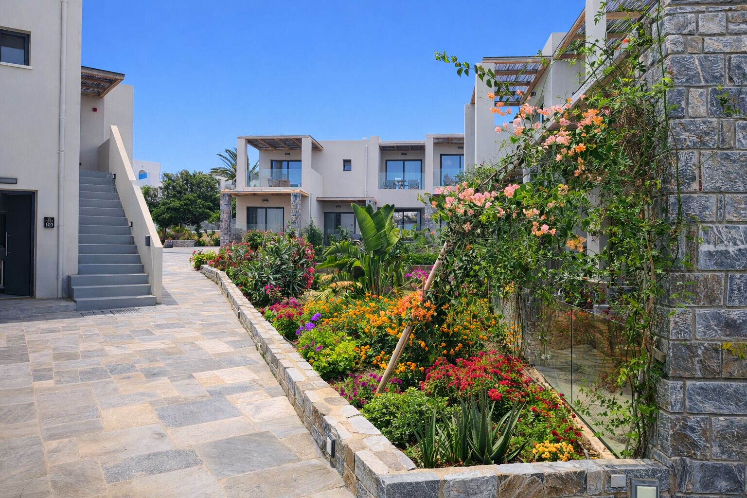Un edificio moderno con facciata in pietra, una scalinata che conduce all'ingresso e una varietà di piante e fiori colorati.