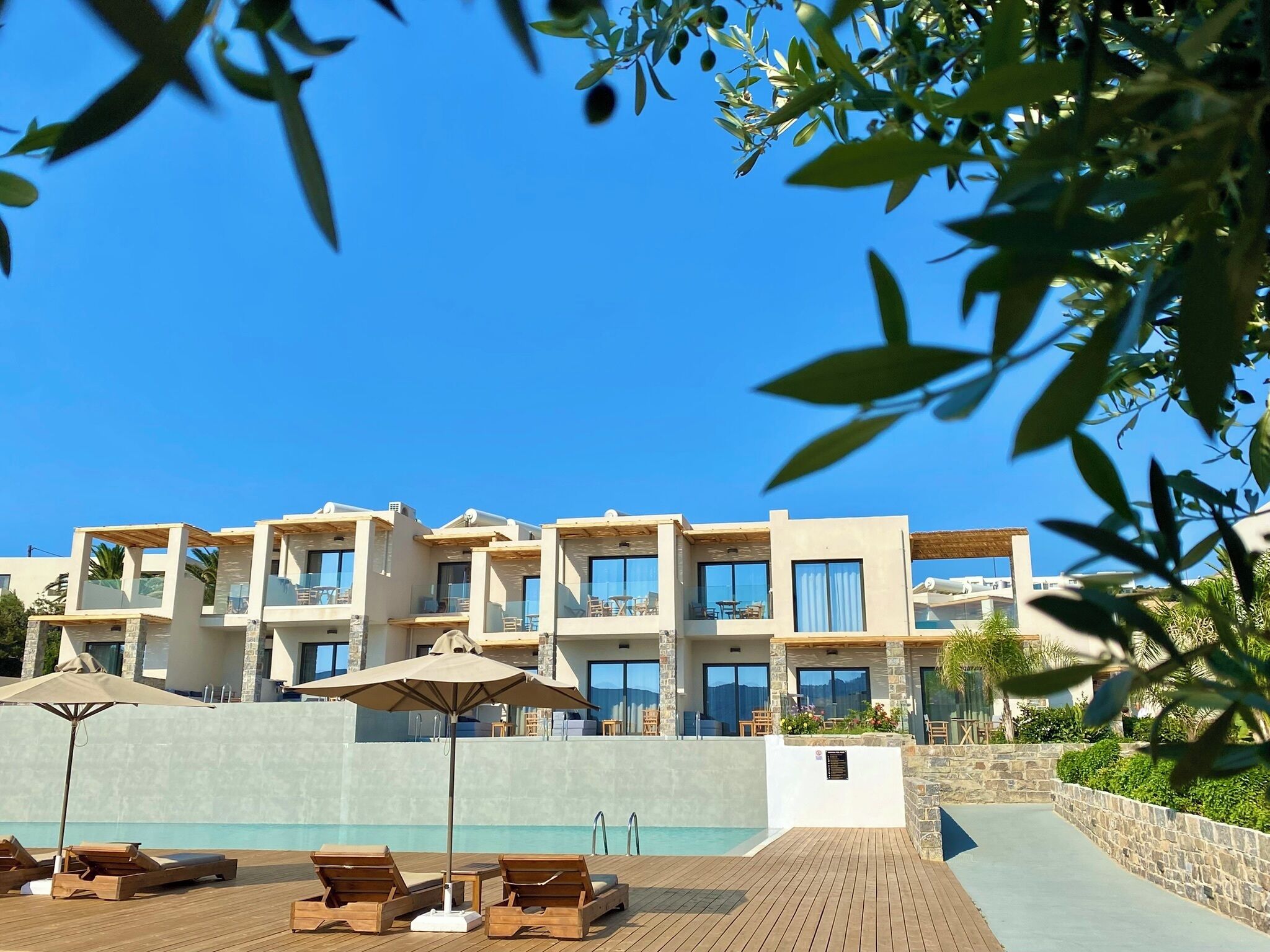 A modern hotel with a pool, wooden lounge chairs, and a clear blue sky.