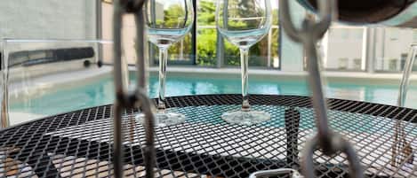Two empty wine glasses on a metal table near a pool.