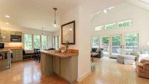 A spacious kitchen with a large island, wooden flooring, and a view of the outdoors through large windows. - Wonderland Home | 2BR retreat, mins to Acadia NP (Tremont)